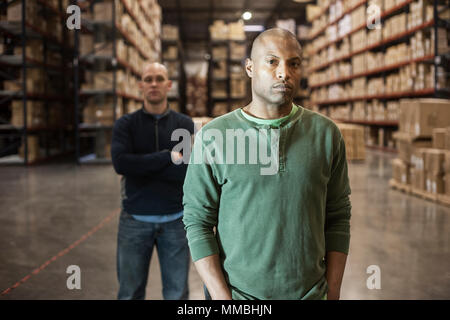 Portrait of an African American and caucasian warehouse workers in a large distribution warehouse with racks of products stored in cardboard boxes on  Stock Photo