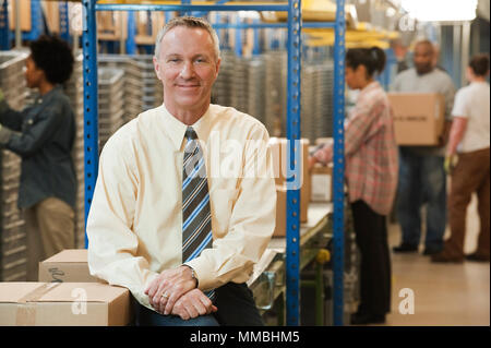 Portrait of a male caucasian executive in a dress shirt and tie  next to a motorized converyor system in a large distribution warehouse. Stock Photo