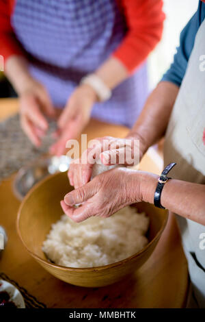 Close up of woman standing at a table in a kitchen, making sushi. Stock Photo