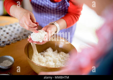 Close up of woman standing at a table in a kitchen, making sushi. Stock Photo