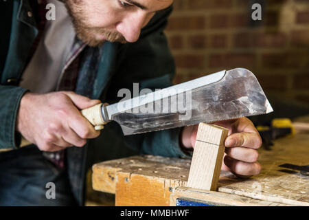 Close up of man working standing in a woodworking workshop, using saw on piece of wood. Stock Photo