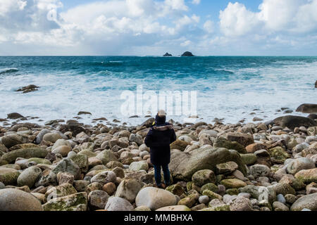 A woman standing on the rocks looking out over the Cornish coastline, and breaking waves. Stock Photo
