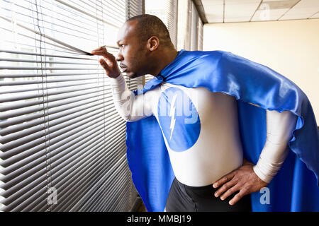 A black businessman office super hero looks out the window and checks his next business move. Stock Photo