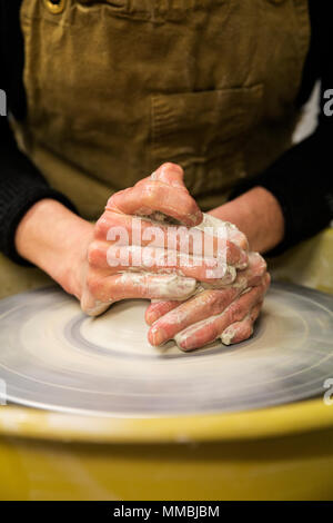 Close up of potter wearing apron working on pottery wheel, shaping clay. Stock Photo