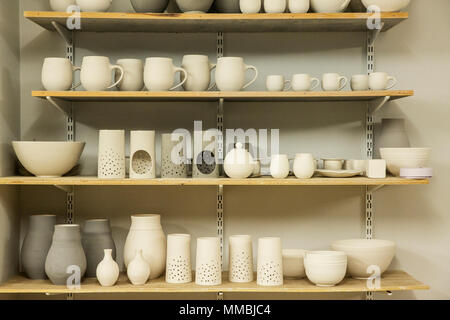 Racks of hand thrown hand crafted pottery vases and objects on shelves in the drying room. Stock Photo