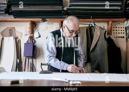 Tailor with measuring tape around neck working with material at bench Stock Photo