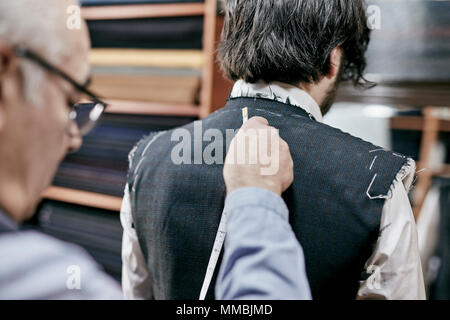 Tailor using measuring tape on a suit jacket, fitting the garment on a customer Stock Photo