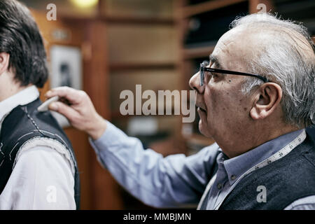 Tailor fitting a jacket on a customer using tailor's chalk to mark the fabric  mature man grey hair glasses client bespoke tailoring Stock Photo