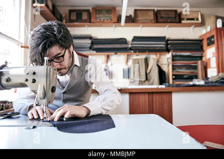 Man sewing a garment using an industrial sewing machine, at a family tailoring business workshop. Stock Photo