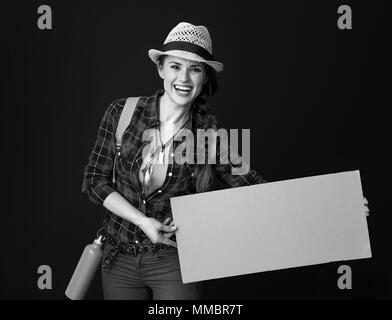 Searching for inspiring places. happy young traveller woman with backpack showing blank board against background Stock Photo