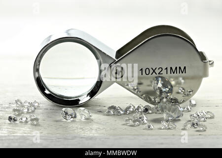 brilliant cut diamonds with folding magnifier on wooden background Stock Photo