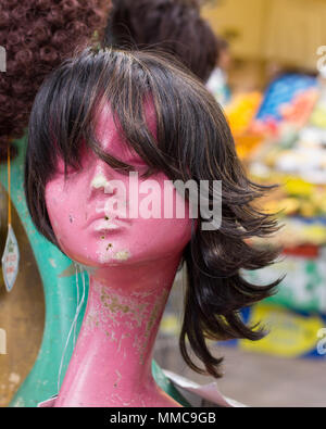 A wig perched on a female mannequin head in the store window display of a Brixton covered market ladies' hair fashion supply business, London, UK. Stock Photo