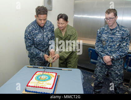 PORTLAND, Ore. (Oct. 13, 2017) — Information Systems Technician Seaman Apprentice Laderlynn Griffin, a native of Philadelphia, Miss., and Military Sealift Command Electronics Technician Roberto Ames, cut the cake for the U.S. Navy's 242nd Birthday on the mess decks on board the submarine tender USS Frank Cable (AS 40), Oct. 13. A sword is used to cut the cake as a reminder that Sailors are a band of warriors, committed to carrying arms so that our nation may live in peace.  The Theme of the Navy's Birthday is, 'Sea Power to Protect and Promote.” (U.S. Navy photo by Mass Communication Specialis Stock Photo