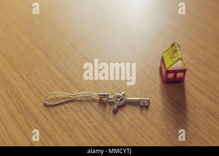A small toy house made of paper and a key lie on a wooden table Stock Photo