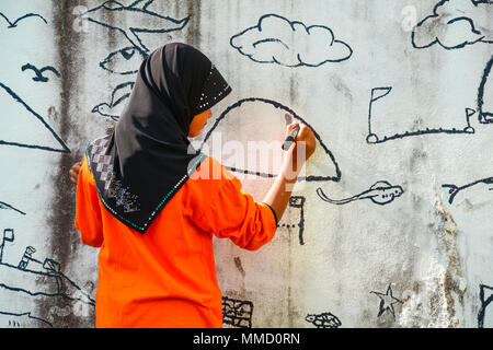 Krabi, Thailand - May 3, 2015: Muslim girl wearing black hijab drawing graphic image on wall of ruined house in Krabi, Thailand Stock Photo