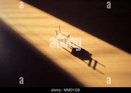 small chair on a wooden floor in a dark room with a stream of bright light from a corner Stock Photo