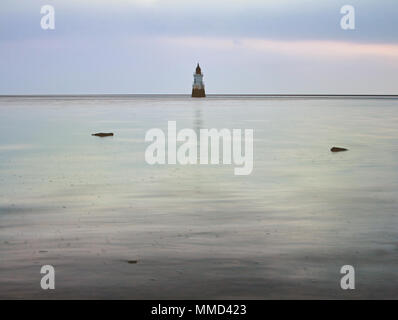 The incoming tide surrounds Plover Scar lighthouse late in the evening Stock Photo