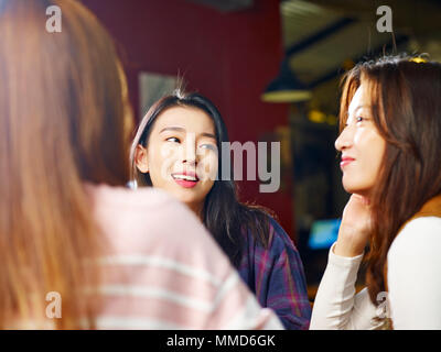 three happy beautiful young asian women sitting at table chatting talking in coffee shop or tea house. Stock Photo