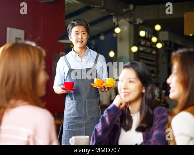 young asian waiter serving female customers in coffee shop, shot through window glass. Stock Photo