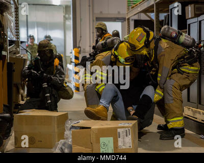 Firefighters from Marine Corps Air Station (MCAS) Iwakuni move a simulated casualty to a new location during a chemical exposure drill while a Japan Ground Self-Defense Force Soldier posts security as part of exercise Active Shield at MCAS Iwakuni, Japan, Oct. 18, 2017. Active shield is an annual exercise that tests the abilities of U.S. and Japanese forces to work alongside each other to protect and defend the air station and other U.S. assets in the region. (U.S. Marine Corps photo by Lance Cpl. Stephen Campbell) Stock Photo