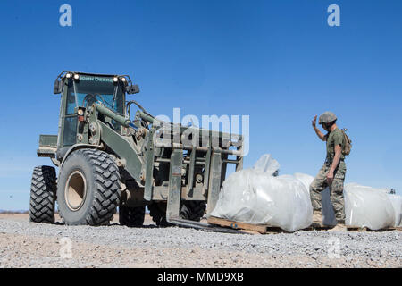 U.S. Marine Corps Pfc. Myles Bautista, an engineering equipment operator with Marine Wing Support Squadron 272 (MWSS-272) ground guides Pfc. Ashley Hewes, an engineering equipment operator with MWSS-272, while she lifts a bag of asphalt with a Tractor, Rubber Tired, Articulated, Multipurpose vehicle (TRAM) during expeditionary airfield maintenance in support of Weapons and Tactics Instructors course (WTI) 2-18 at STOVAL Expeditionary Airfield, Dateland, Ariz., March 14, 2018. WTI is a seven-week training event hosted by Marine Aviation Weapons and Tactics Squadron One (MAWTS-1) cadre, which em Stock Photo