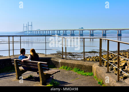 Two people on seat overlooking Severn Estuary with M4, Second Severn Crossing bridge Stock Photo