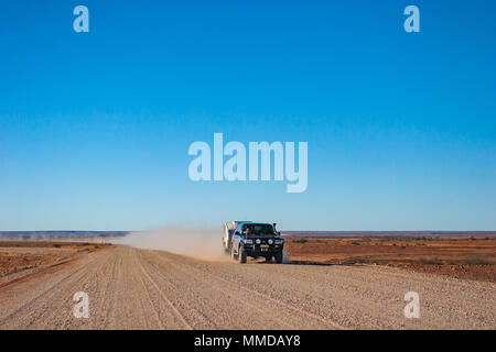 Four wheel drive vehicle towing a pop-top caravan over a dirt road with trailling dust cloud. Stock Photo