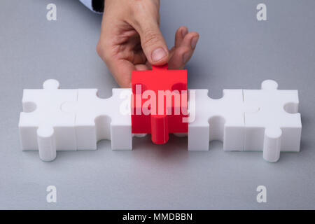 A Person's Hand Placing Red Piece Between White Jigsaw Puzzle Stock Photo