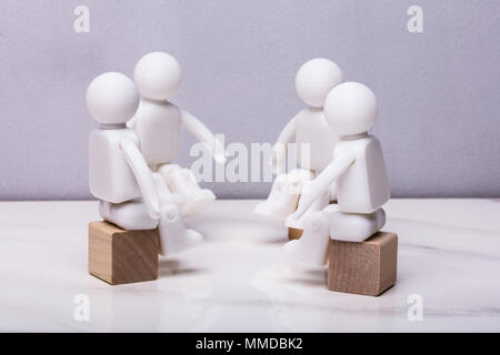 Four White Human Figurines Sitting On Wooden Block Having Meeting Together Stock Photo