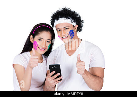 Happy Two Teenage Couple Holi Festival Showing Thumbs-up With Mobile-Phone Stock Photo