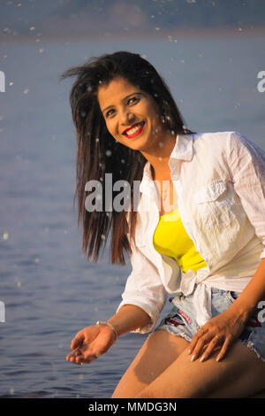 Smiling woman in yellow top, white jacket and denim shorts with water drops on face Stock Photo