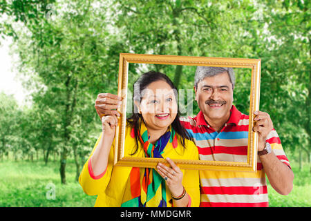 Happy Two Senior Couple holding picture frame Over face. In Garden Stock Photo