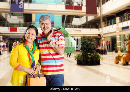 Happy Senior Couple Standing Together Carrying Shopping Bags In-Mall Stock Photo