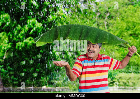 Happy Senior Man under Banana-Leaf putting hand out to feel raindrops on palm Stock Photo