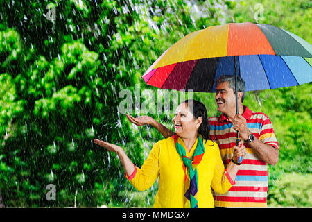 Happy Senior Couple under umbrella putting-hand out to feel raindrops,Palm Stock Photo