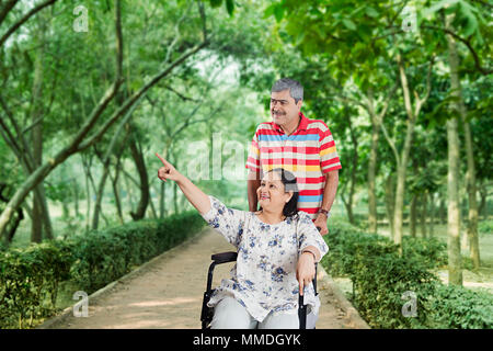Elderly Couple Enjoying Their Walk In-Park, Woman Being In Wheelchair Stock Photo