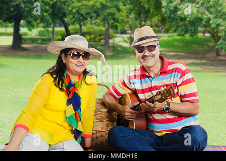 Two Senior Lovers couple in love having picnic in-park with guitar Stock Photo