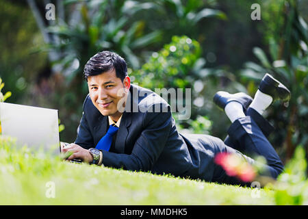 One Business male Executive Lying Grass Resting Laptop Working In-Garden Stock Photo