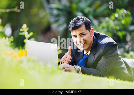 One Businessman Employee Lying-Grass Showing Thumbs-up And Laptop Working Garden Stock Photo