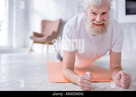 Charming senior man smiling while doing plank Stock Photo