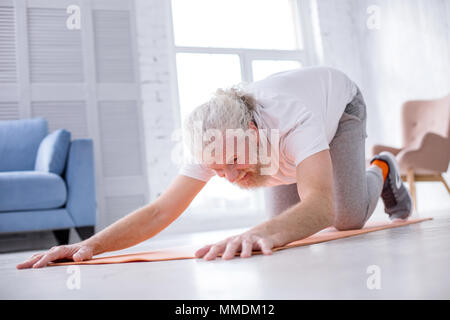 Grey-haired senior man practicing extended puppy pose at home Stock Photo
