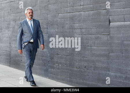 Senior businessman walking outside of modern office building. Successful business man wearing suit and tie in urban background. Stock Photo