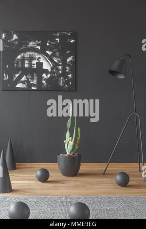 Cactus, painting on the black wall and metal lamp surrounded by cones and balls on the floor in artistic interior Stock Photo