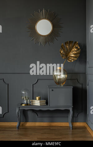 Decorative mirror above a gray retro cabinet with a golden plant leaf in a dark luxurious apartment interior with molding Stock Photo