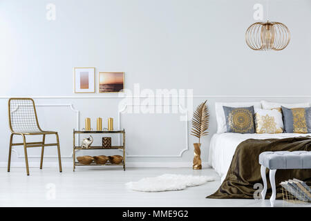 Gold accents in bedroom interior with bed, chair, metal shelf and modern lamp Stock Photo