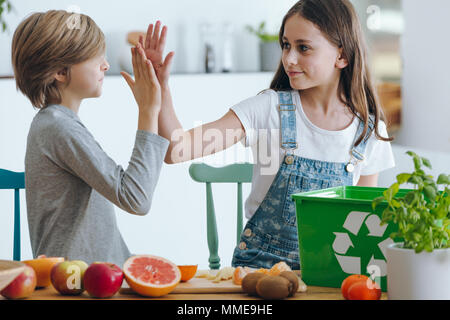 Siblings high fiving while segregating biodegradable waste in the kitchen Stock Photo