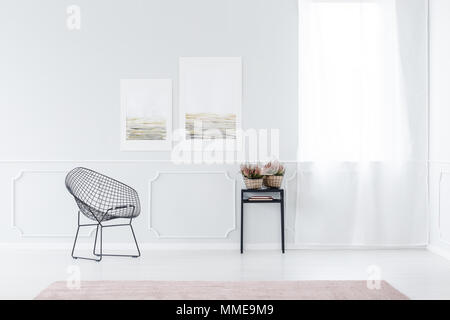 Elegant office interior with black, metal chair and table with heathers against white wall with molding in the waiting area Stock Photo