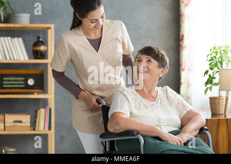 Concerned caregiver checking up on her elder patient in cozy retirement home on a sunny day Stock Photo