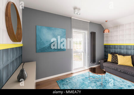 Trendy sophisticated interior with copper coffee table, abstract painting, turquoise rug, mirror, gray couch and yellow details Stock Photo
