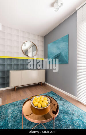 Black and white square molding with yellow detail on wall in modern colorful living room with sideboard, painting, copper coffee table and turquoise r Stock Photo